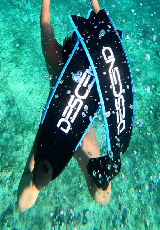 Diver kicking down through turquoise water in black Descend fins with blue side rails